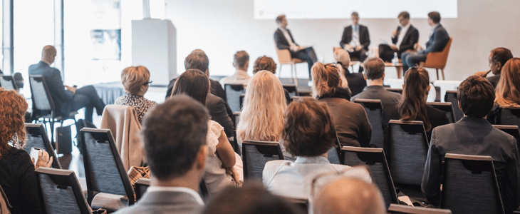 a crowd of people watch guest speakers on a stage