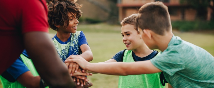 A group of young soccer players put their hands in a circle