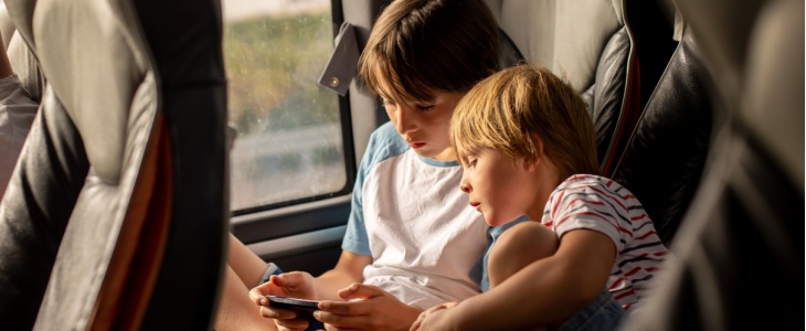 Two kids on a bus look at a tablet