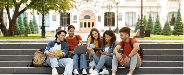 A group of teens sits on the steps of a college campus