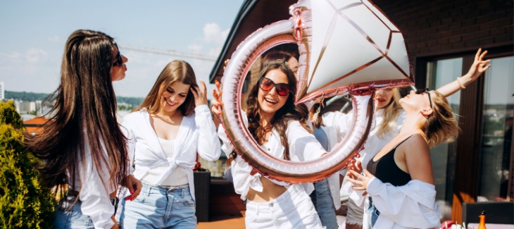 An excited bride holds up a large foil balloon at her bachelorette party